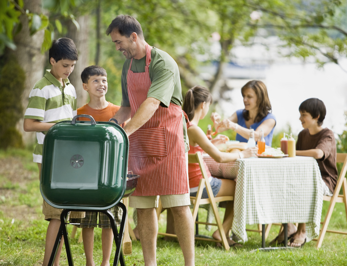 Father and son (10-14) tending barbecue, family in background