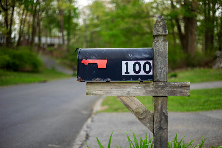 Black mailbox with number 100 on white fixed on wooden stand at road on American countryside.