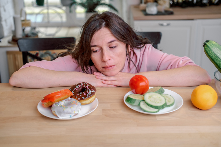 Young woman chooses between sweet donuts and fresh vegetables, healthy eating