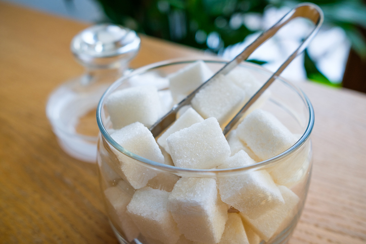 Lump sugar in a transparent glass sugar bowl, on a wooden table or background, at home, in a cafe, cafeteria or restaurant. The concept of poor nutrition and lifestyle.
