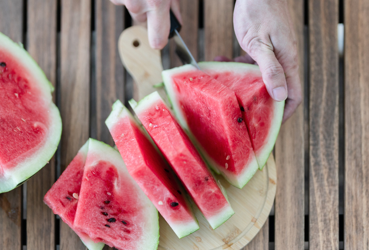 Close-Up Of Man Cutting Watermelon Slices On Table