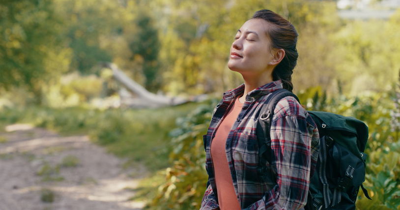 Deep breath hiking woman in nature, forest trees or jungle in zen meditation to relax, calm and peace of mind. Happy girl breathing fresh air on backpack holiday adventure or woods trekking travel