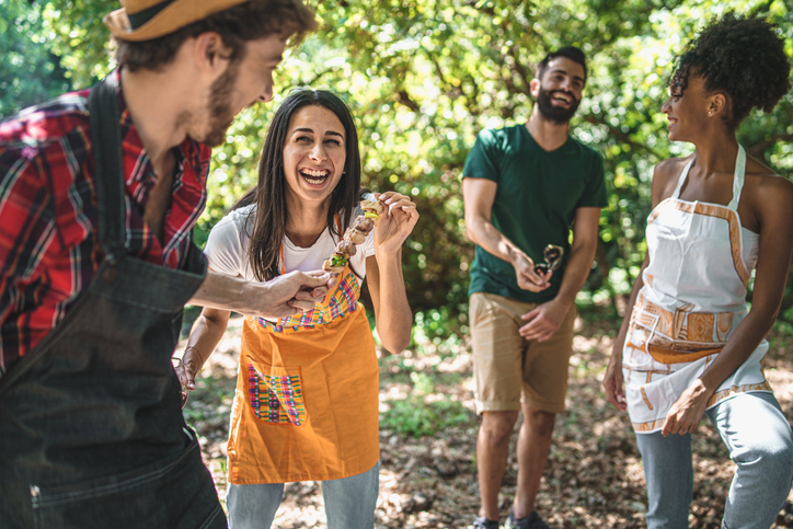 Group of young friends grilling skewers outdoors having fun together at the countryside