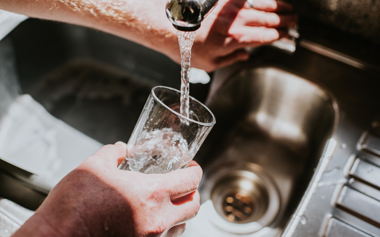A man pours a glass of water from a chrome tap at a kitchen sink
