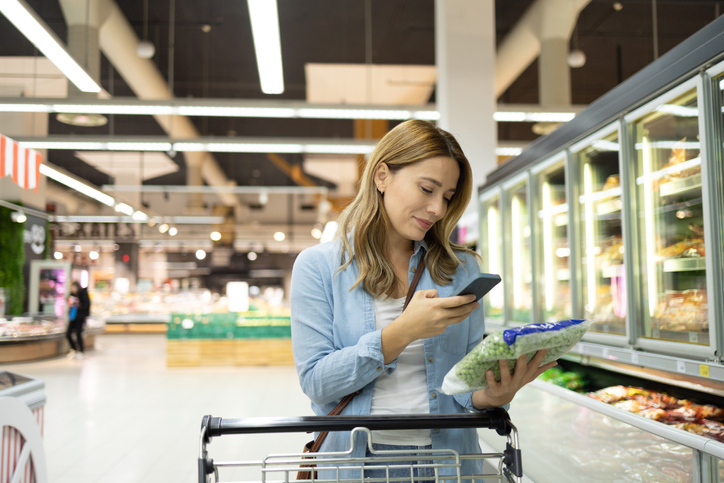 Young woman checking shopping list on smart phone in supermarket