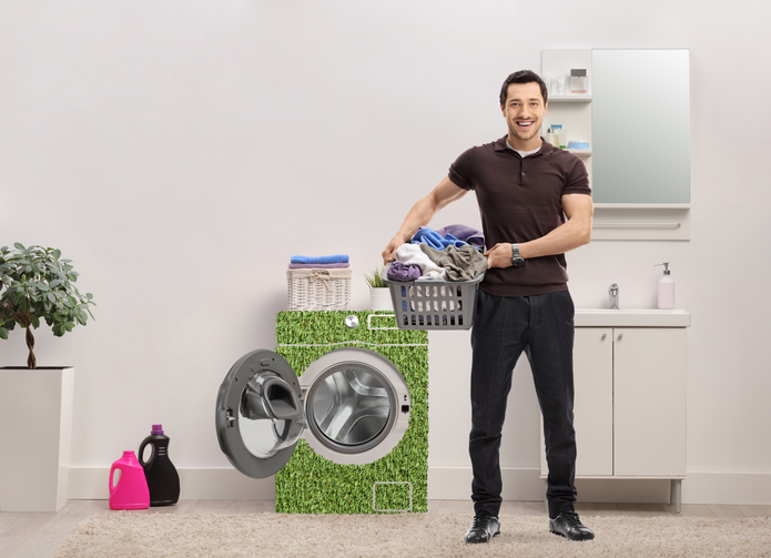 Man with a laundry basket full of clothes standing in a bathroom next to energy efficient waching machine