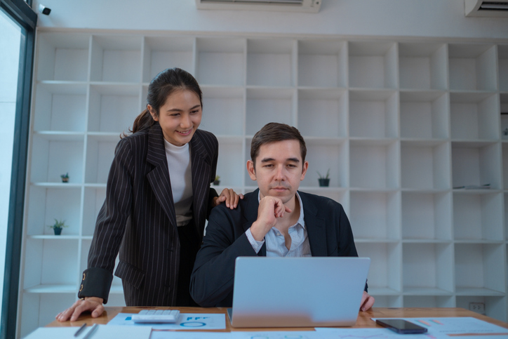 Two business people using a laptop in an office, a man and a women analyzing documents stat at office