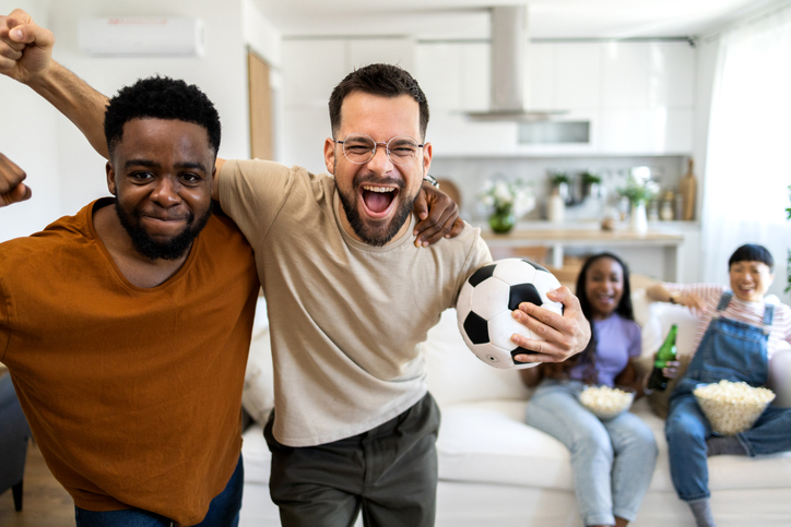 Group of cheerful friends shouting while watching a sports game on TV at home