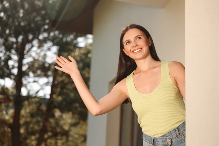 Neighbor greeting. Happy woman waving near house outdoors
