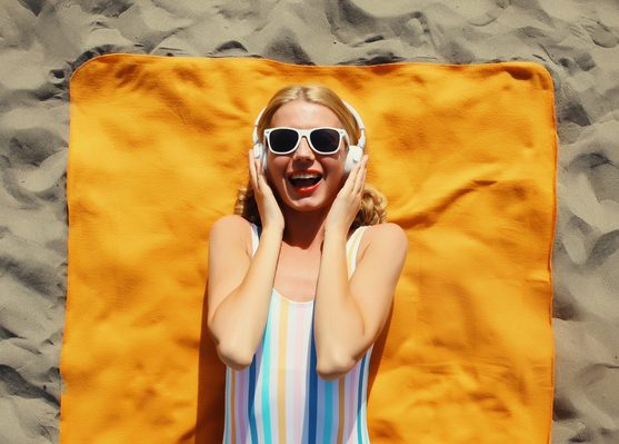 Summer vacation, happy cheerful woman listening to music lying on the beach, relaxed girl on towel
