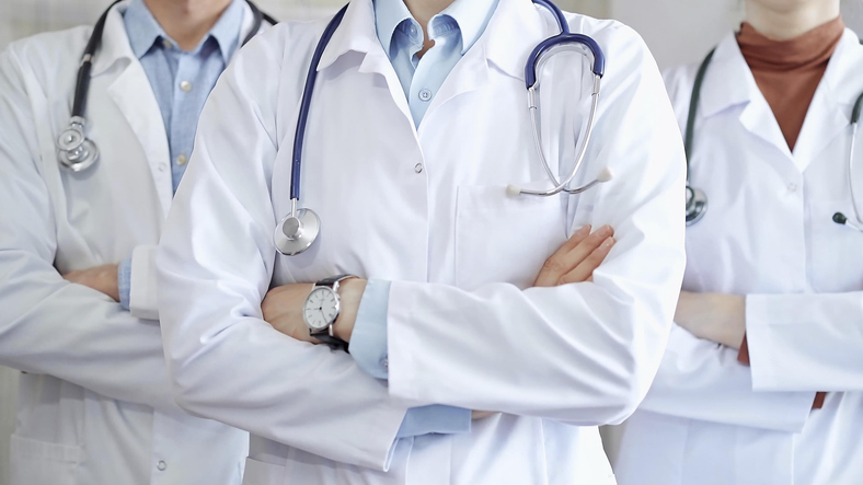 Group of doctors wearing white coats and stethoscopes standing with arms crossed. Medical team at work