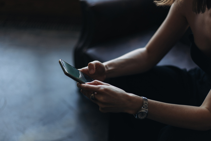 Young woman using smartphone on a black sofa.