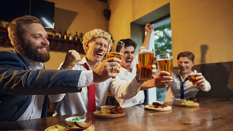 Group of men, colleagues raise their glasses in celebratory toast, filled with energy and excitement.