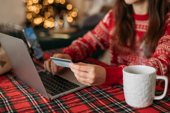 Christmas sales and online shopping. Hand with credit card on laptop with blank screen at table on background of stylish Christmas decorations, gifts and Christmas tree. Black Friday sale