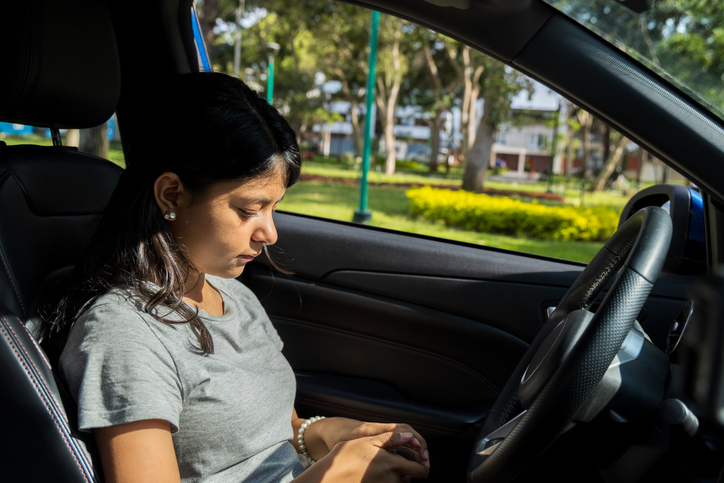 A teenager is sitting in a car and looking at the ground