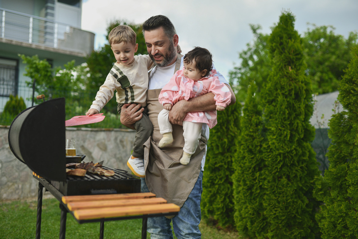 Tender Father Embracing Daughter And Son While Cooking Barbecue Outside