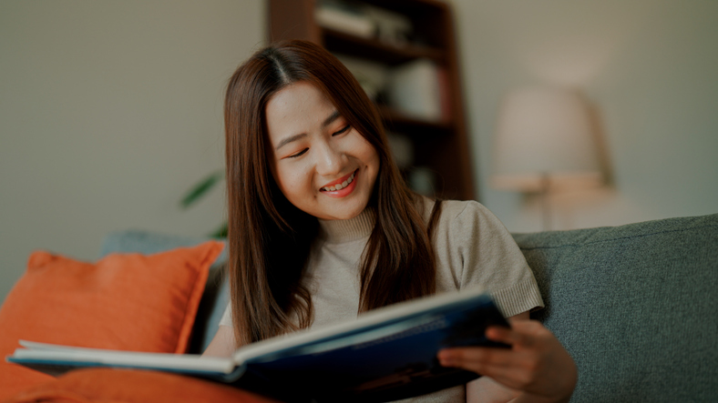 Young Asian woman looking at pictures in a book while reading peacefully.