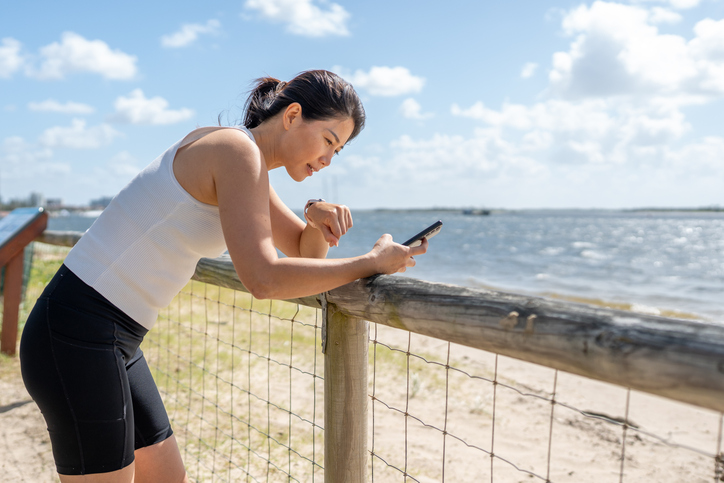 Asian Woman Leaning on Fence Using Smartphone