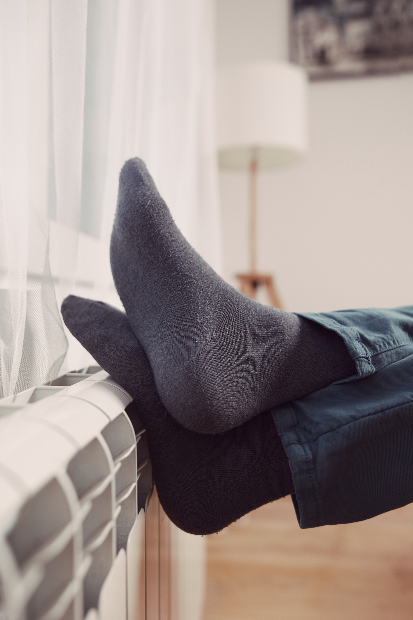 Man's feet with socks on a home heating radiator on a cold winter day outdoors.
