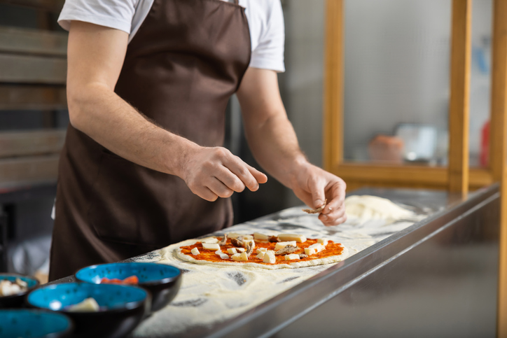 Man rolls dough in kitchen flattening carefully preparing pizza base