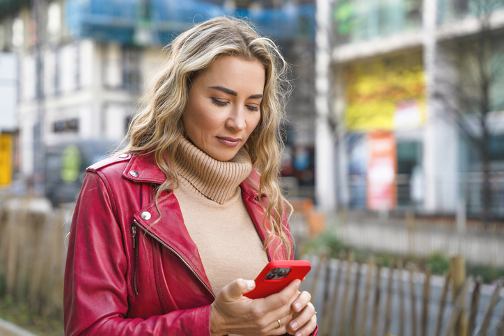 Woman in red jacket checks phone on the street in a city during daytime in a busy area