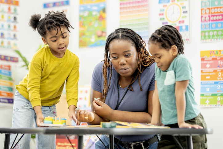 Black Female Teacher Engaging Two Young Black Students in Hands-On Learning Activity in Colorful Classroom